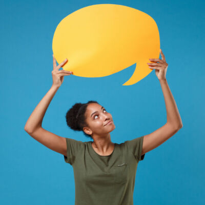 Pretty young african american woman girl in casual t-shirt posing isolated on bright blue background. People lifestyle concept. Mock up copy space. Hold yellow empty blank Say cloud, speech bubble.